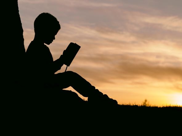 a boy reading a book alone on a field